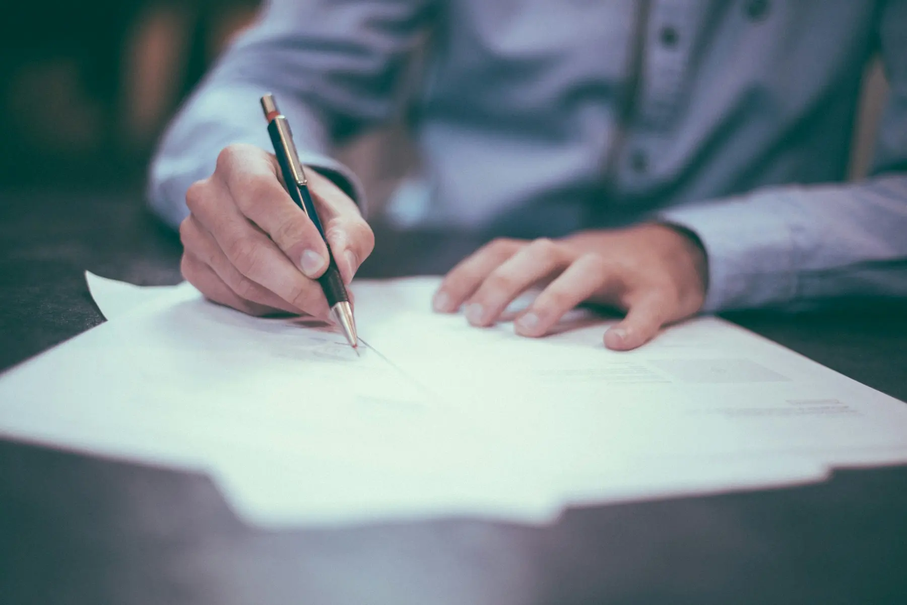 A person signing a document at a desk, illustrating a commercial-insurance renewal decision.