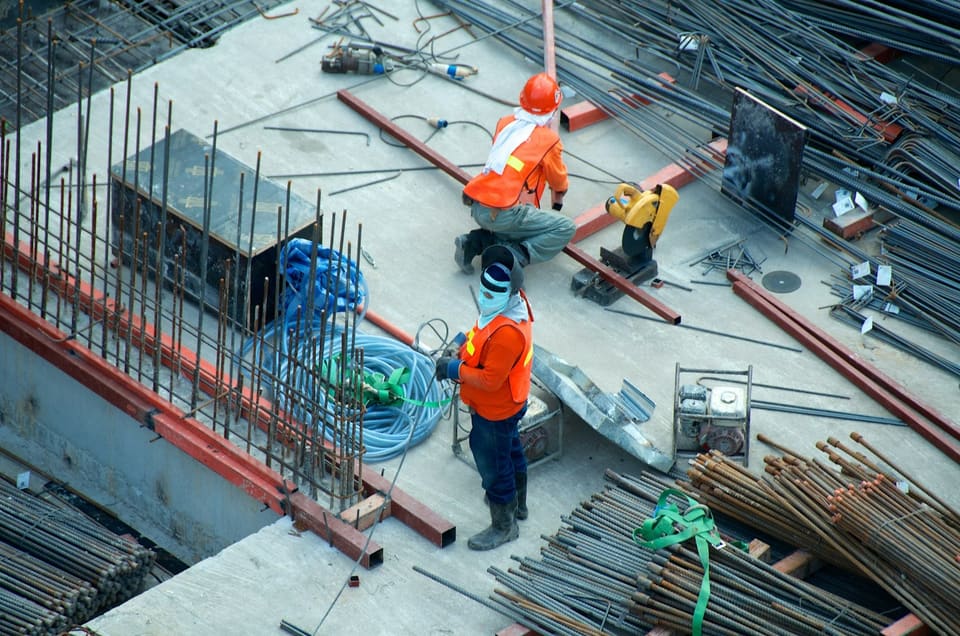 Two workers in high-visibility vests on a concrete deck laid with reinforcing bar and steel beams.