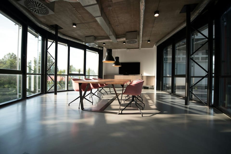 A meeting table and chairs in a glass-walled office with an exposed concrete ceiling.