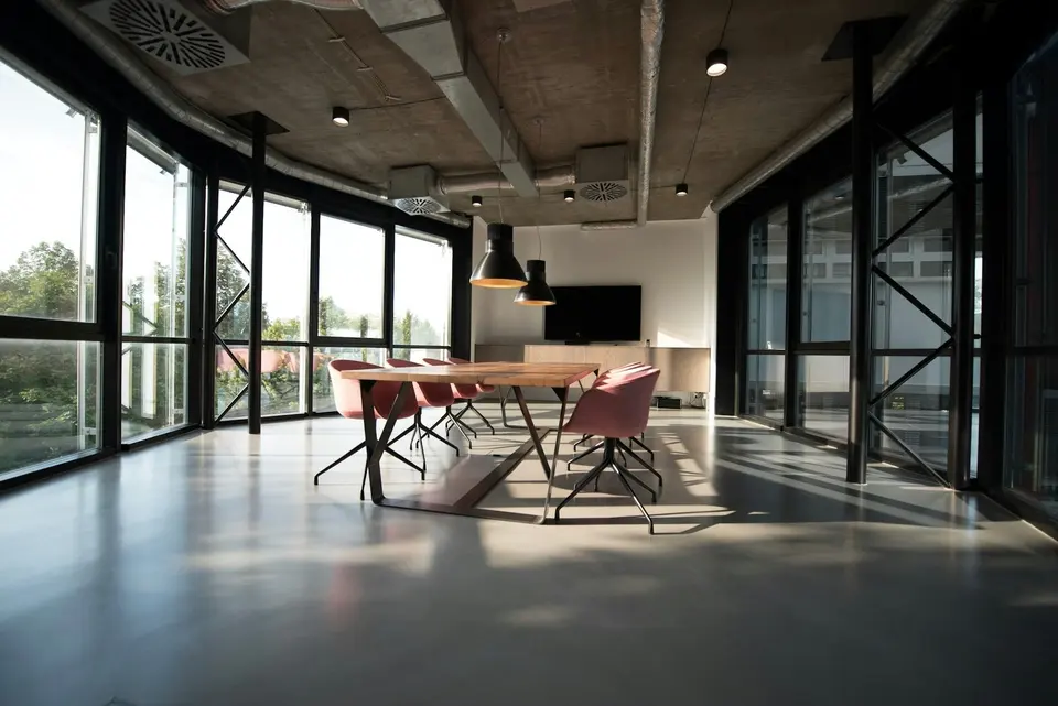 A meeting table and chairs in a glass-walled office with an exposed concrete ceiling.