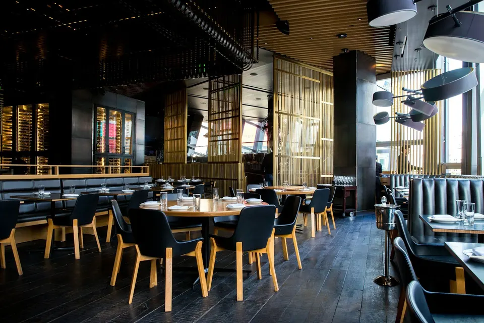 An empty restaurant dining room with set tables, banquette seating and pendant lights.
