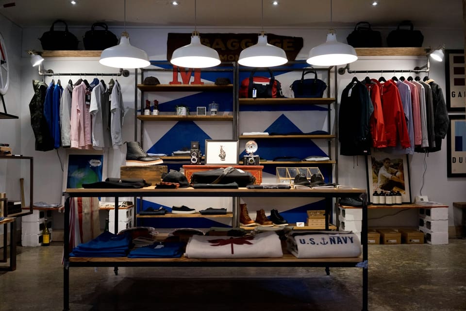 Clothing, bags and accessories displayed on open shelving and rails in a small shop.